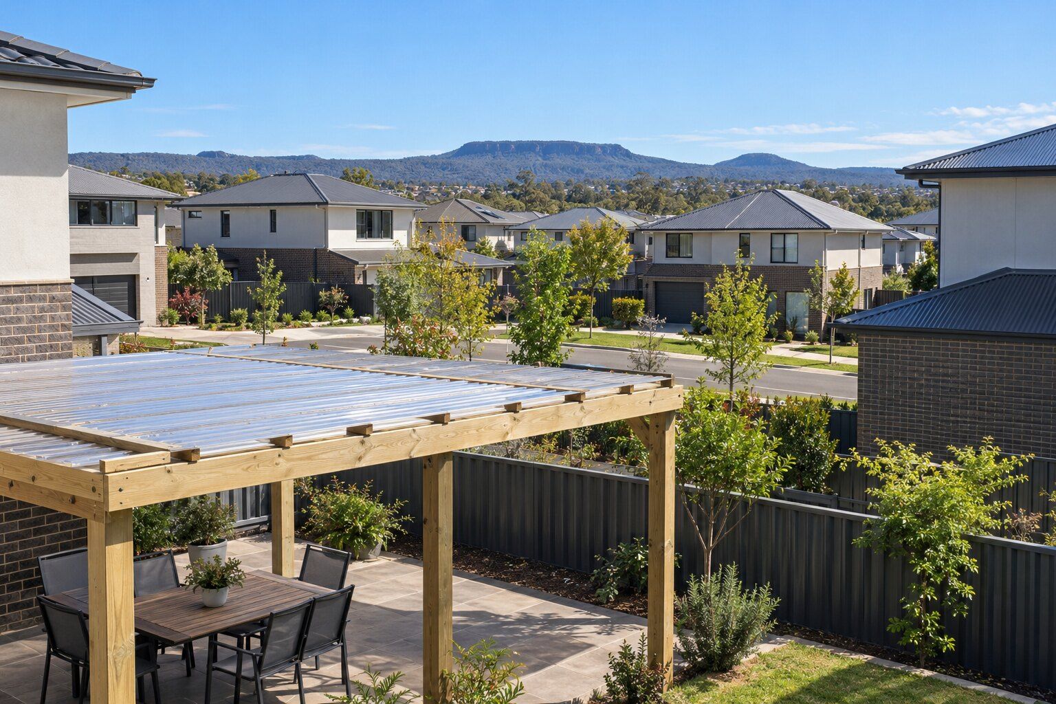 Carpenter, Gungahlin: a timber pergola with a clear corrugated roof over a paved patio, looking across a new estate of two-storey homes towards distant hills