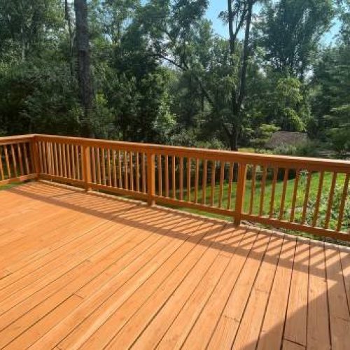 A wooden deck with a set of sliding glass doors providing an unobstructed view of a lush green tree in the near distance